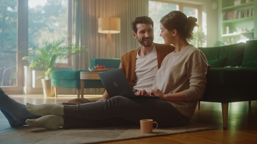 Couple Use Laptop Computer, Do High-Five in Celebration, while Sitting on the Living Floor room of their Apartment. Boyfriend and Girlfriend Talk, Shop on Internet, Choose Product to Order Online Royalty-Free Stock Footage #1070801011