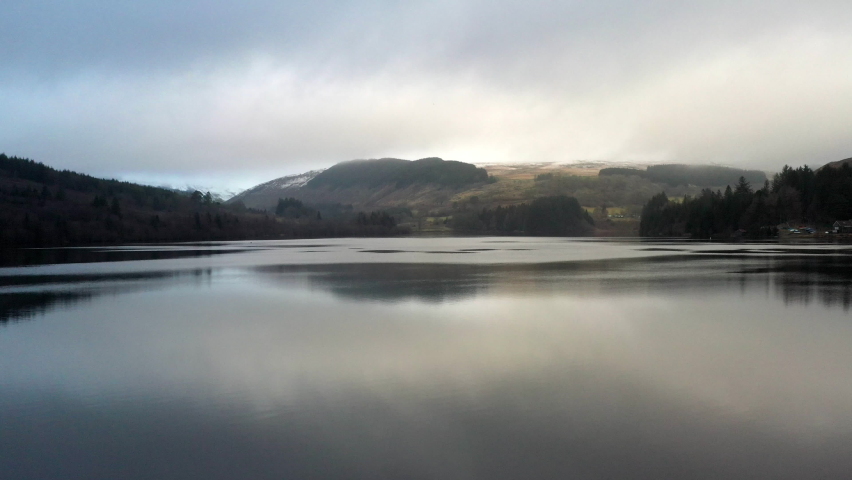 Glassy still mountain lake with reflections on winter evening with sun going down behind the hills. Beautiful evocative scenery of the Brecon Beacons in Wales, UK. Beautiful Britain.