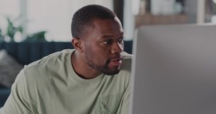 African American Casual Guy Watching Fun Video Content on Computer Monitor Screen Staring Curiosly Staying Home in Apartment. Entertainment.