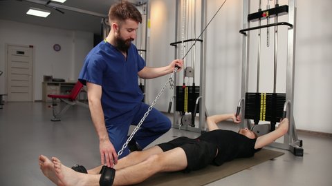 Athlete male patient in clinic sport physical therapy concept. Occupational therapist helping ailing. Physiotherapist doing exercise for knee. Physician treating injured leg
