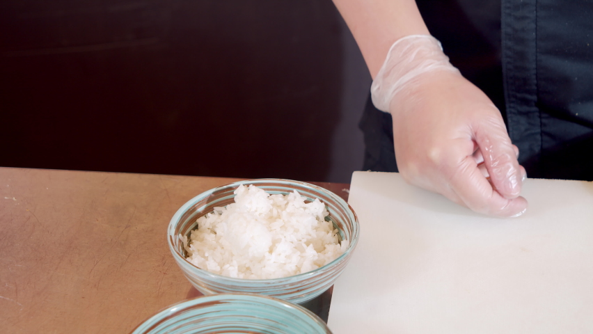 Hand of a cook in a glove crumpling rice while preparing a base for sashimi in the kitchen.