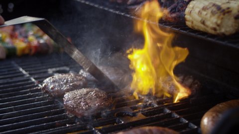 Huge flames shoot up around delicious charred burgers at a bbq