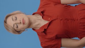Tired, sleepy young brunette woman in red shirt yawning widely, feeling exhausted and lazy, suffering from insomnia. Indoor studio shot isolated on blue background.Video for the vertical story.