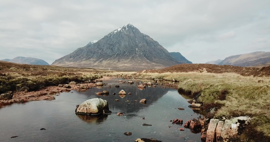 Buachaille Etive Mor and Rannoch Moor in Scottish Highlands. Aerial footage over River Coe with mountain reflected in water. Lifting upwards to show panoramic view of landscape. Royalty-Free Stock Footage #1070818105