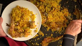 Spanish cook hands serving delicious Valencian rice paella on plate