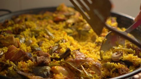 Cook with kitchen tools on paellon of Valencian paella handling the food