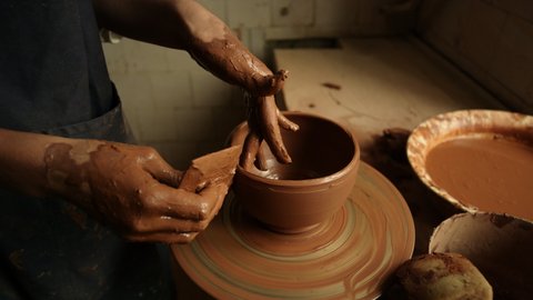Unrecognized woman sculpting clay pot in workshop. Closeup lady making product on potters wheel in studio. Unknown girl working with wet clay in pottery.