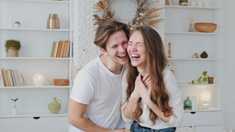 Young caucasian couple married man and woman millennials standing together embracing posing, funny guy boyfriend blow puffing out cheeks holding breath girl girlfriend laughing sincerely loudly smile