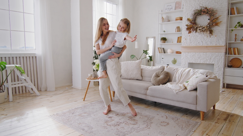 Young happy mother caucasian mommy babysitter woman holding in arms hands toddler little daughter child kid small girl dancing together in living room to music whirl spinning sing song having fun Royalty-Free Stock Footage #1070834245