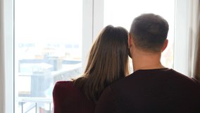 Dreamy young couple homeowners hugging standing indoors looking out window. Husband and wife first time home buyers feels happy, share dreams planning common future. 4 k video