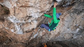 slow motion top view woman rock climber climbs on overhanging crag by tough challenging route and clipping rope in quickdraws. challenge lead climbing on natural rocks