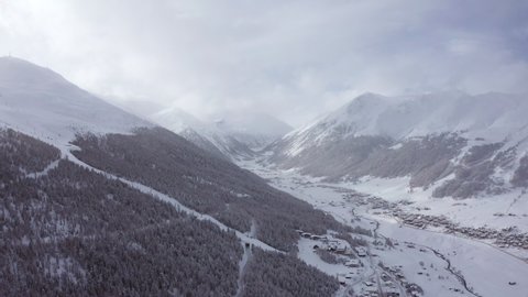 Drone clip of Livigno, magical winter destination for your holidays in Italy, clouds and a light snowfall, with sun flares