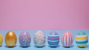 Video of Happy Easter. Colorful painted Easter eggs roll and knock each other on a blue and pink background. Hello spring and easter concept. 4k video.