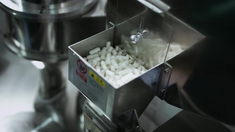 White pills capsules in the manufacture of medicines and medical supplies. Automatic production line, a machine for creating dietary supplements and vitamins. Medical factory or plant.