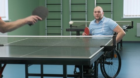 A man with a physical disability who uses a wheelchair plays ping pong. People with disabilities play table tennis. Paralympic sport.