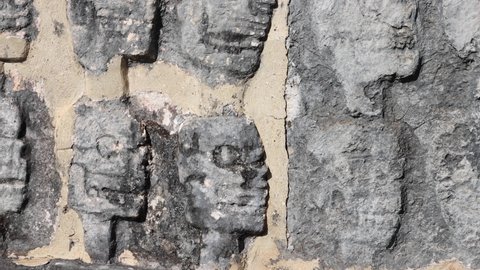 Details on the wall in a mayan archeological site in Mexico, human skulls shaped on the stones referencing mayan human sacrifices. Day light scary ruins. Adventurous vibe.