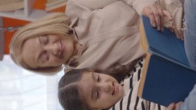 The granddaughter and grandmother sitting on the sofa are reading a fairy tale book. Grandmother and grandchild activity concept.Slow motion and close up video.Video for the vertical story.