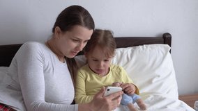 caucasian family little children girl and young woman mom talking in video conference by smartphone together at home with happiness smile on white bed. technology, lifestyle, mobile phone use concept