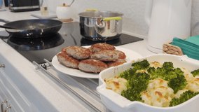 Cooking meals for dinner in modern white clean kitchen, frying cutlets and baked vegetables. High quality 4k footage