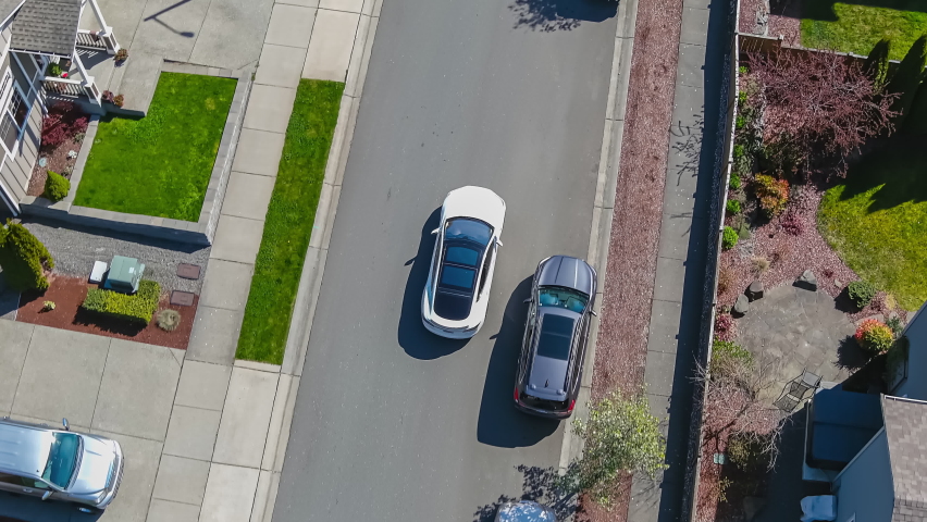 Aerial view of a white car driving through a suburban neighborhood arriving at home; drone follow shot Royalty-Free Stock Footage #1070874550