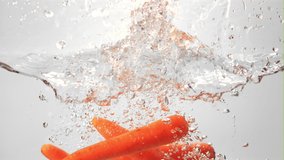 Super slow motion ripe carrots with spray falls into the water. On a white background. Filmed on a high-speed camera at 1000 fps. High quality FullHD footage