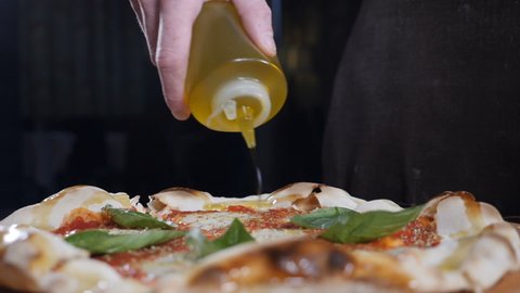 Pouring adding olive oil to ready handhmade pizza. Traditional Italian pizza. cheese and basil. pizza with tomato sause and mozzarella, traditional food in italy, high kitchen gastrobar restaurant
