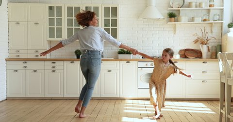 Woman and small daughter listen music dancing indoor, active mom hold in hands lifting kid spinning enjoy funny playtime on weekend in cozy modern sunlit kitchen. Fun, happy homeowners, tenant concept