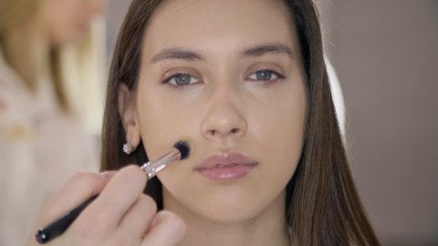 Close-up of a woman having her face covered with a foundation. Make-up specialist improving model's appearance. High quality 4k footage