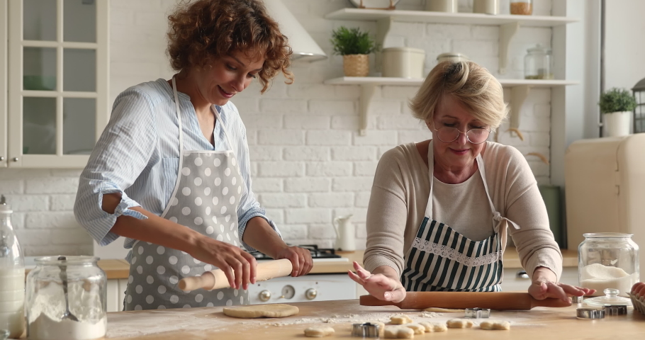 Cheerful older woman her grown up adult daughter talk make flattening dough with rolling-pins in kitchen. Family use ecological products high quality ingredients cooking together laughing feel happy Royalty-Free Stock Footage #1070890879