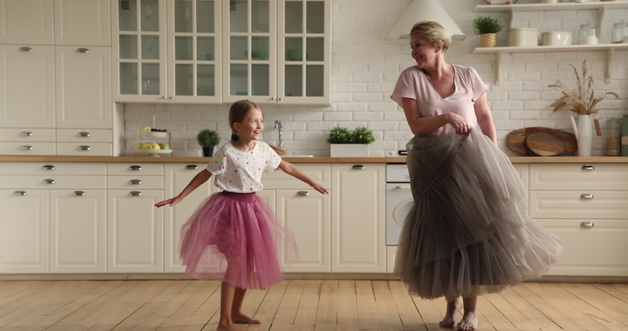 Active elderly 60s grandmother dancing barefoot in wooden floor underfloor heat system with little granddaughter in warm modern kitchen, family listen music having fun together at home. Hobby concept Royalty-Free Stock Footage #1070890882