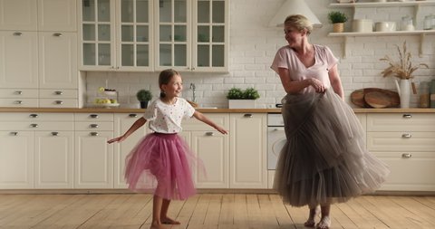 Active elderly 60s grandmother dancing barefoot in wooden floor underfloor heat system with little granddaughter in warm modern kitchen, family listen music having fun together at home. Hobby concept