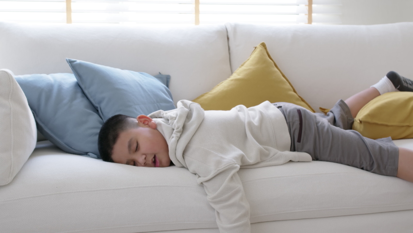 Fatigue in children laying fall down asleep slumber on sofa at home need rest or brain break after virtual study online remote learn at home problem in asian kid feel lack of energy and tired. | Shutterstock HD Video #1070897230