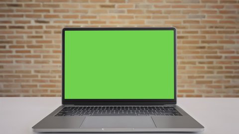 Close up display computer desktop with mock-up green screen on white table, Slow motion laptop green screen on desk and brown brick wall background, Blank of mockup notebook PC, Chroma key monitor.