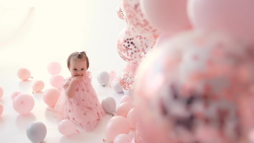 Little cute girl smiling with colorful balloons white and pink in birthday decoration
