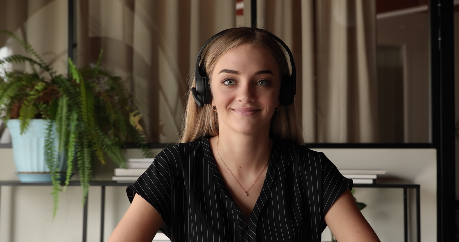 Web camera view smiling young beautiful blonde business lady in wireless headset with microphone looking at camera, holding video call zoom meeting, negotiating working issues with colleagues online. Royalty-Free Stock Footage #1070903821