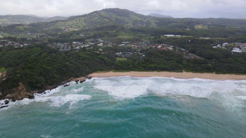 White Bluff Headland With Foamy Waves Onto Shore Of Sapphire Beach In Coffs Harbour, New South Wales, Australia. - Aerial Wide Shot