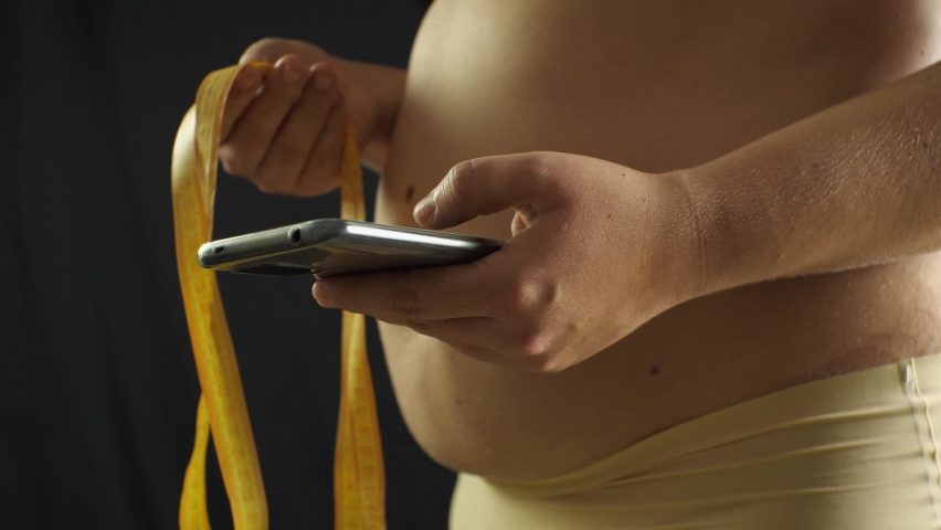 A plus size woman using smartphone with mesaurement tape in the hand. Weight loss concept