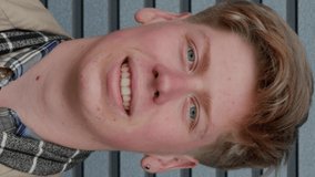 Vertical video of Portrait of young blond boy looking around and after merrily smiling looking at camera against the background of a striped wall. Guy student with blue eyes close up - Powered by Shutterstock - Get 15% off with code: PIKWIZARD15