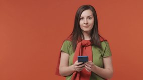 Woman wears basic casual olive green khaki t-shirt get video call using mobile cell phone doing selfie talk conducting pleasant conversation greet with hand isolated on bright orange color background