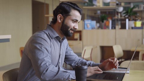 Happy bearded indian business man working on laptop from home office. Male indian executive using computer remote studying, browsing web, having virtual meeting, typing on computer.