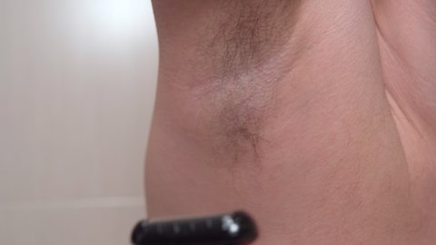 Male depilation. Young man using razor to remove hair from his armpit