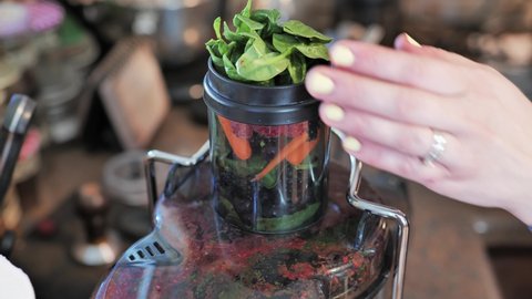 Woman presses fresh organic fruits and vegetables through juicer. Close up.