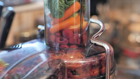 Fruits, berries, and vegetables being pressed into juicer. Close up.