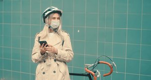 Woman in protective mask, in helmet using her smartphone device. Girl standing on green background.
