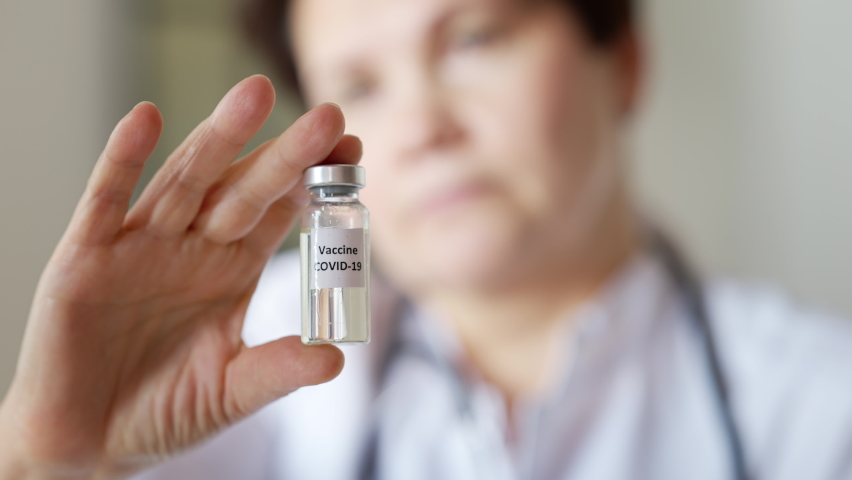 Close-up of coronavirus vaccine jar in female Caucasian hand with blurred face of serious middle aged woman at background. Professional doctor scientist showing Covid-19 treatment indoors Royalty-Free Stock Footage #1070940730