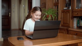 A little cute girl looks at the laptop screen and is excited by luck and success, maybe she won the game or the lottery. Concept of a winner in cyberspace and training for the ps. Child at home indoor
