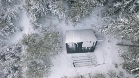 Aerial view of a small house with triangular roof near snow covered trees. Clip. Lonely shelter for extreme hikers or hunters.