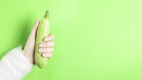 Video 4k hand of a girl in a white fluffy sweater holds a young zucchini moving on a green background copy space for text