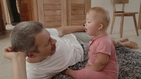 Happy toddler girl down syndrome play with her father at home. Baby shows her daddy funny and emotional grimaces and gestures.