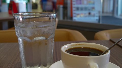 Cup of coffee on a wooden table with glass of water macro video
